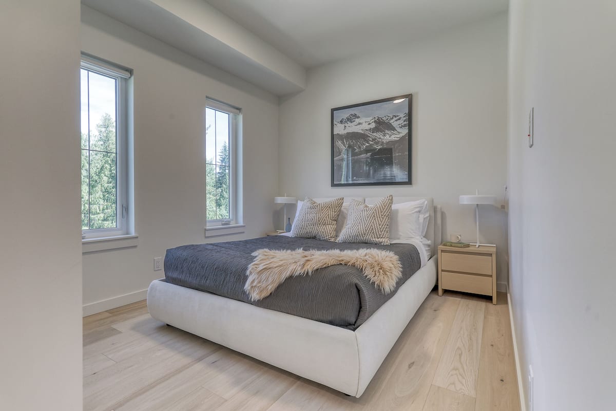 A modern bedroom with a large bed, two bedside tables, a nightstand, and a framed picture on the wall.