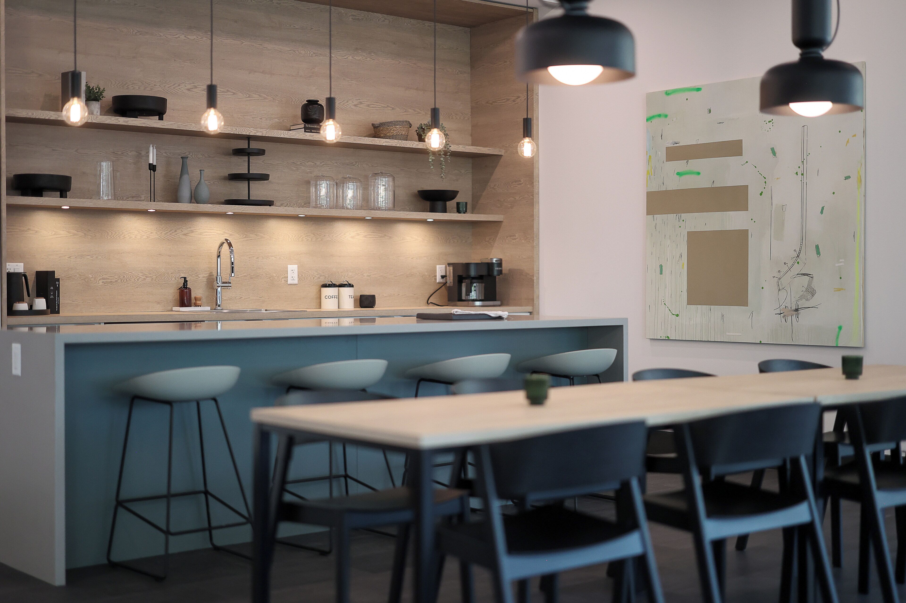 A modern kitchen with a central island, bar stools, pendant lighting, and a coffee machine.