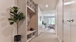 A modern hallway with a plant, a coat rack, and a mirror reflecting a living room with a sofa and a window. - The Crescent (Rossland)