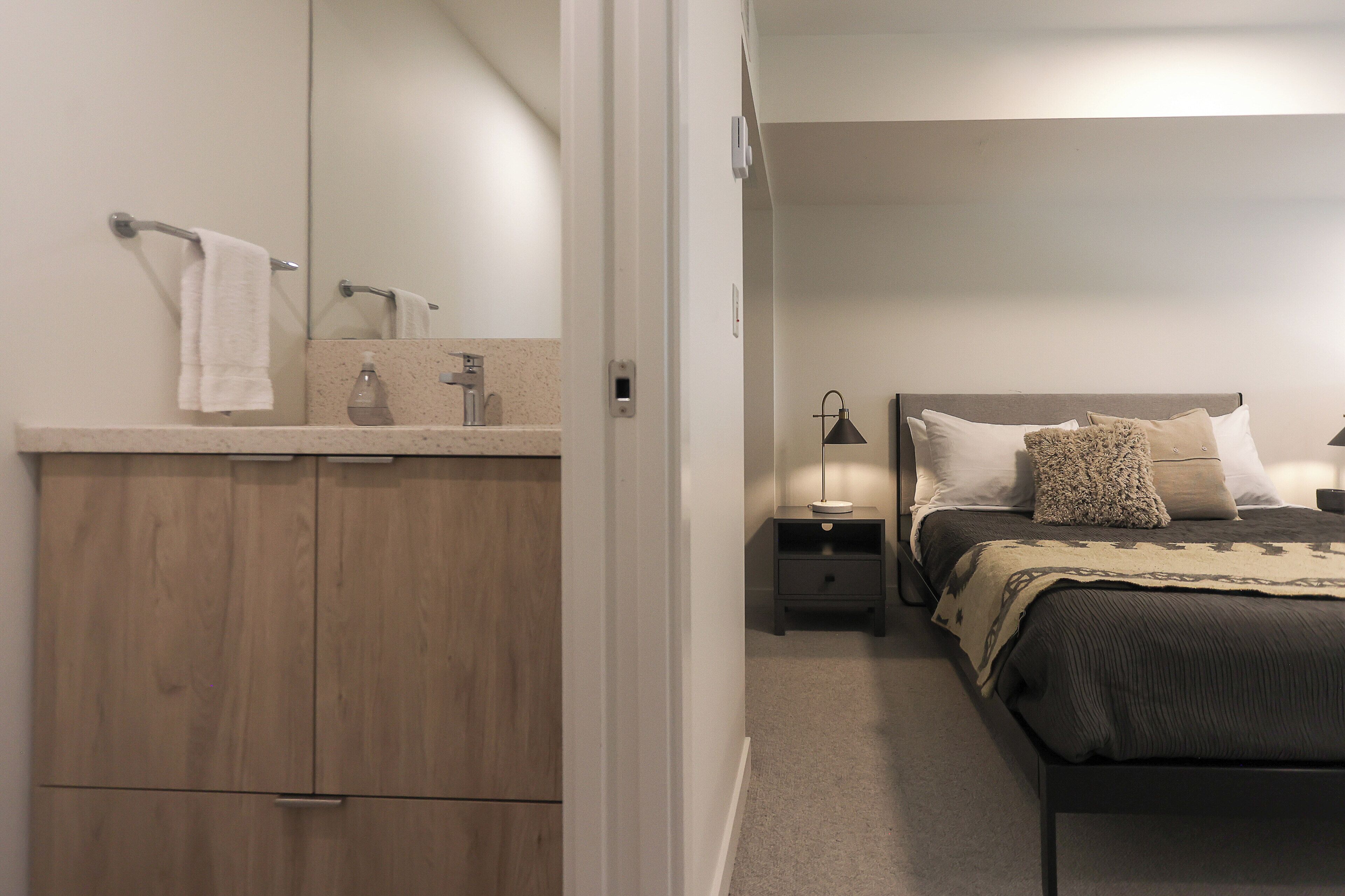 A bedroom with a bed, nightstands, a lamp, a mirror, and a wooden wardrobe.