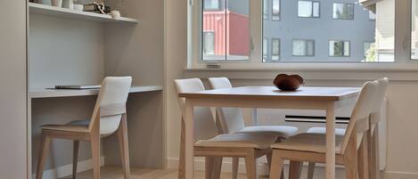 A modern dining area with a white table and chairs, a shelf with decorative items, and a window with a view of buildings.