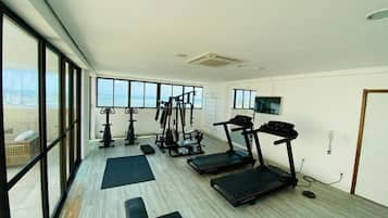 Un gimnasio con equipo de ejercicio, ventanas amplias y vistas a la ciudad.
