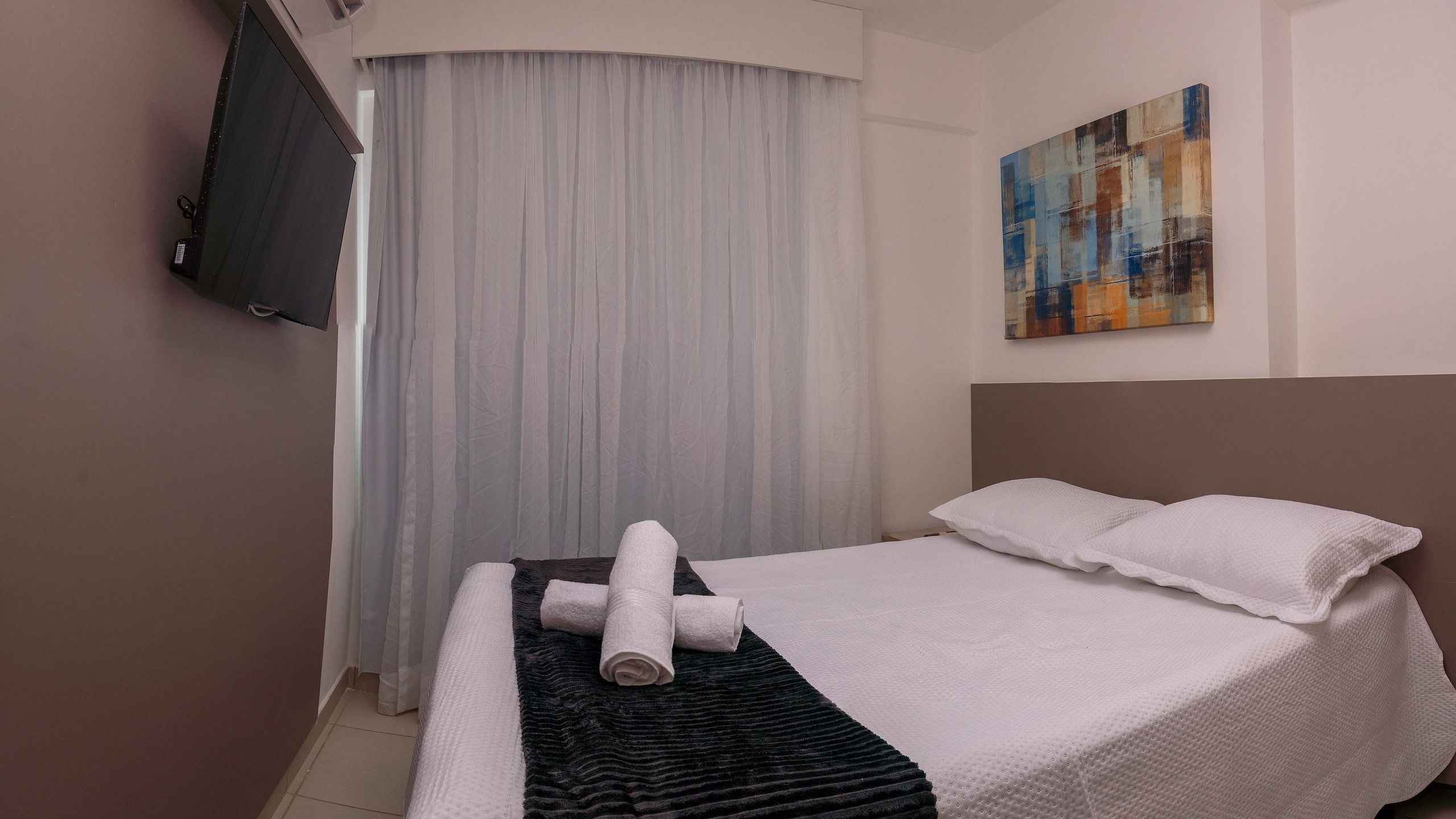 Ein Hotelzimmer mit einem Bett, einem an der Wand befestigten Fernseher und einem Gemälde.