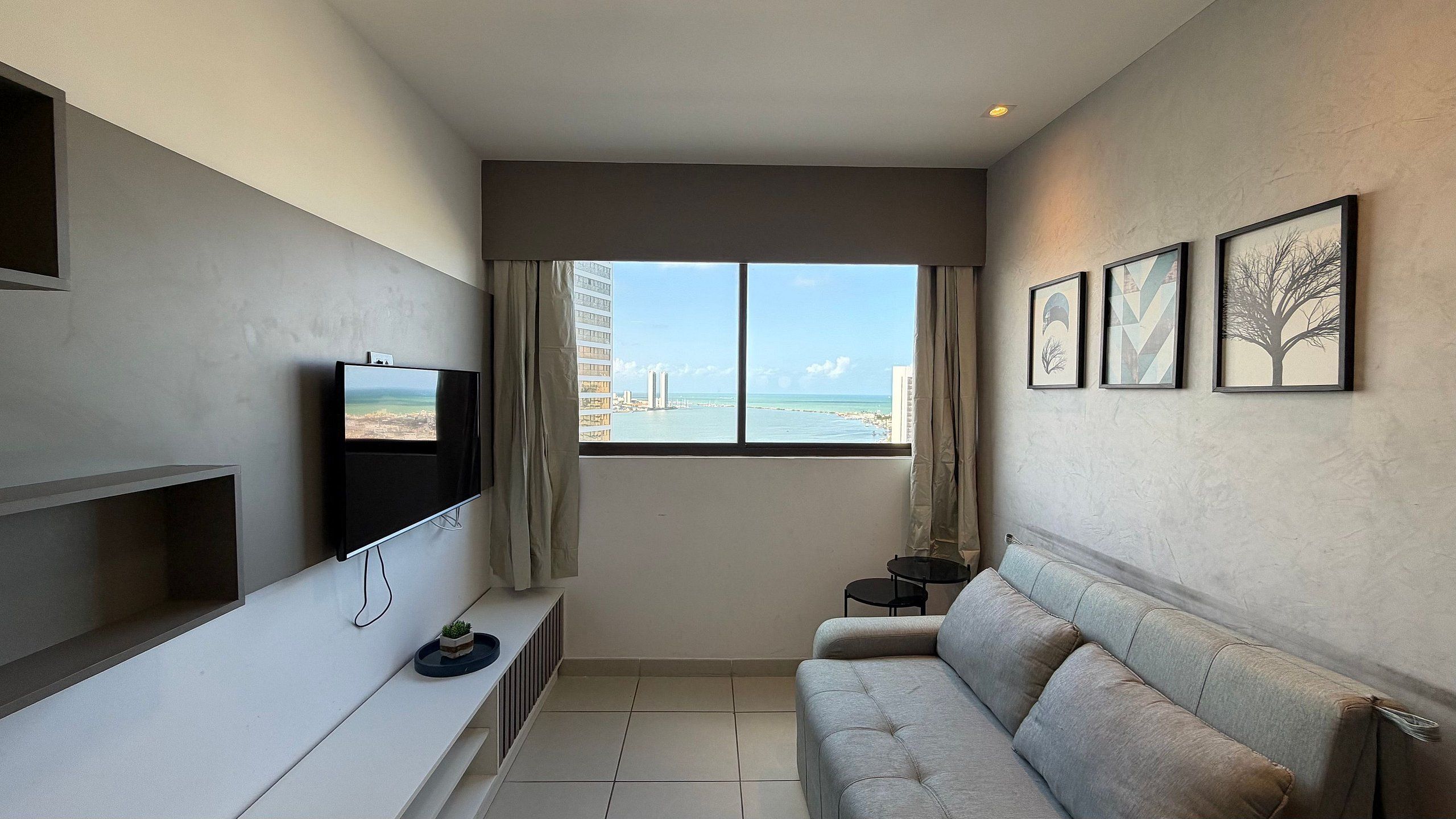 Uma sala de estar moderna com televisão, sofá, mesa pequena e janela com vista para a cidade.