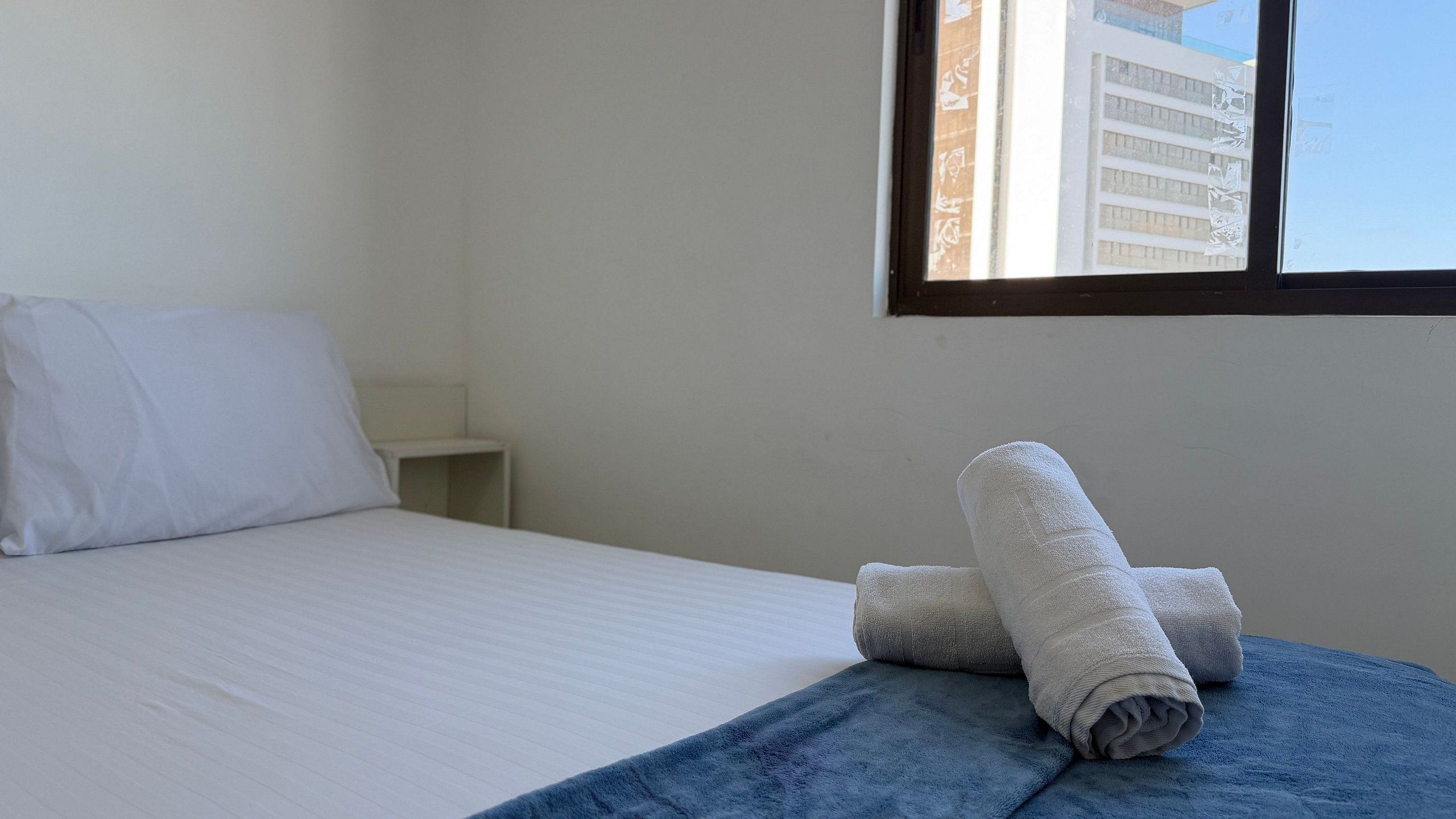 Una habitación de hotel con una cama, una ventana y una toalla doblada sobre la cama.