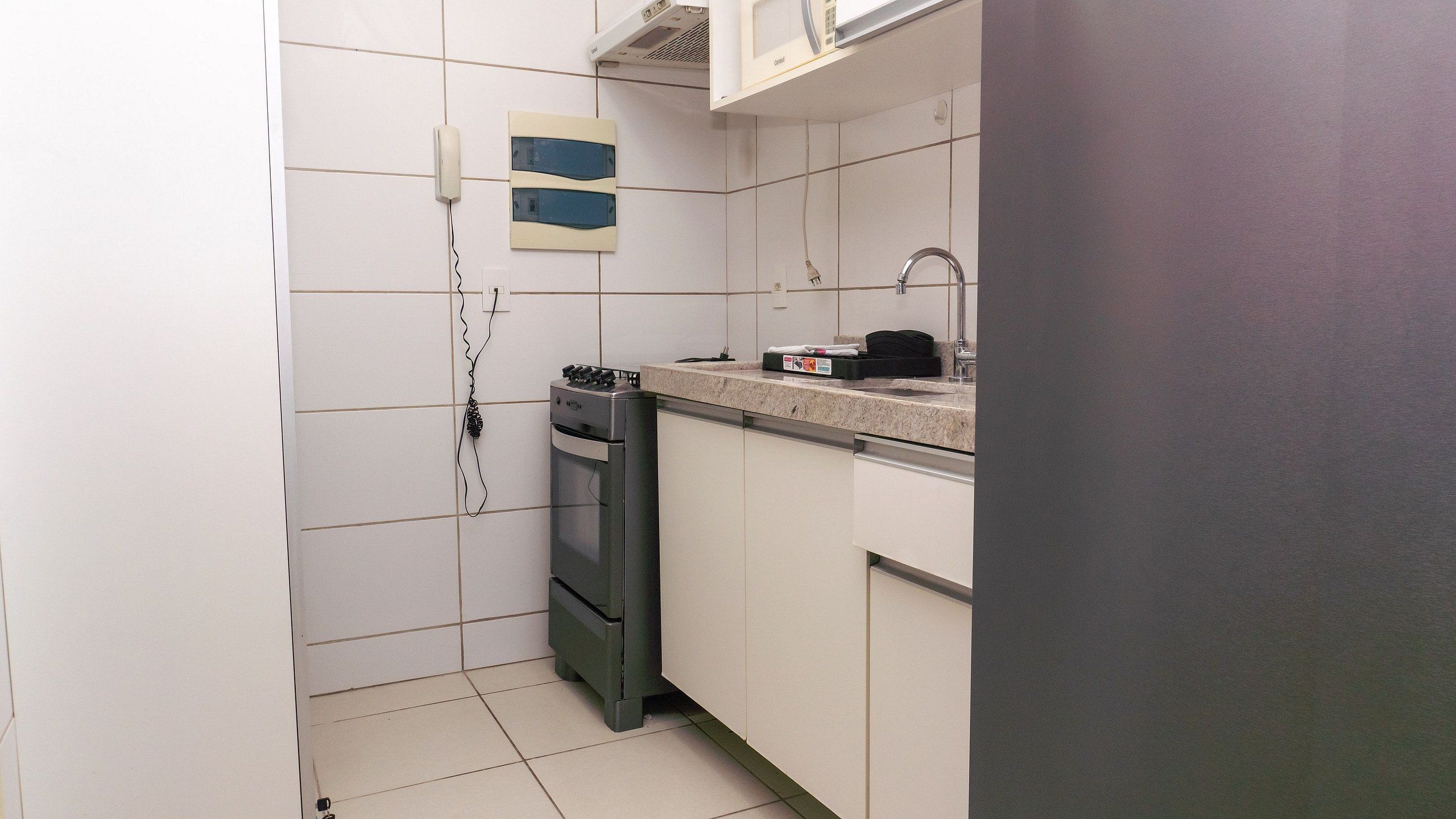 A compact kitchen with white cabinets, a built-in oven, and a microwave on the countertop.