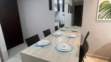A dining area with a long table set for six, modern pendant lights, and a framed plant on the wall.