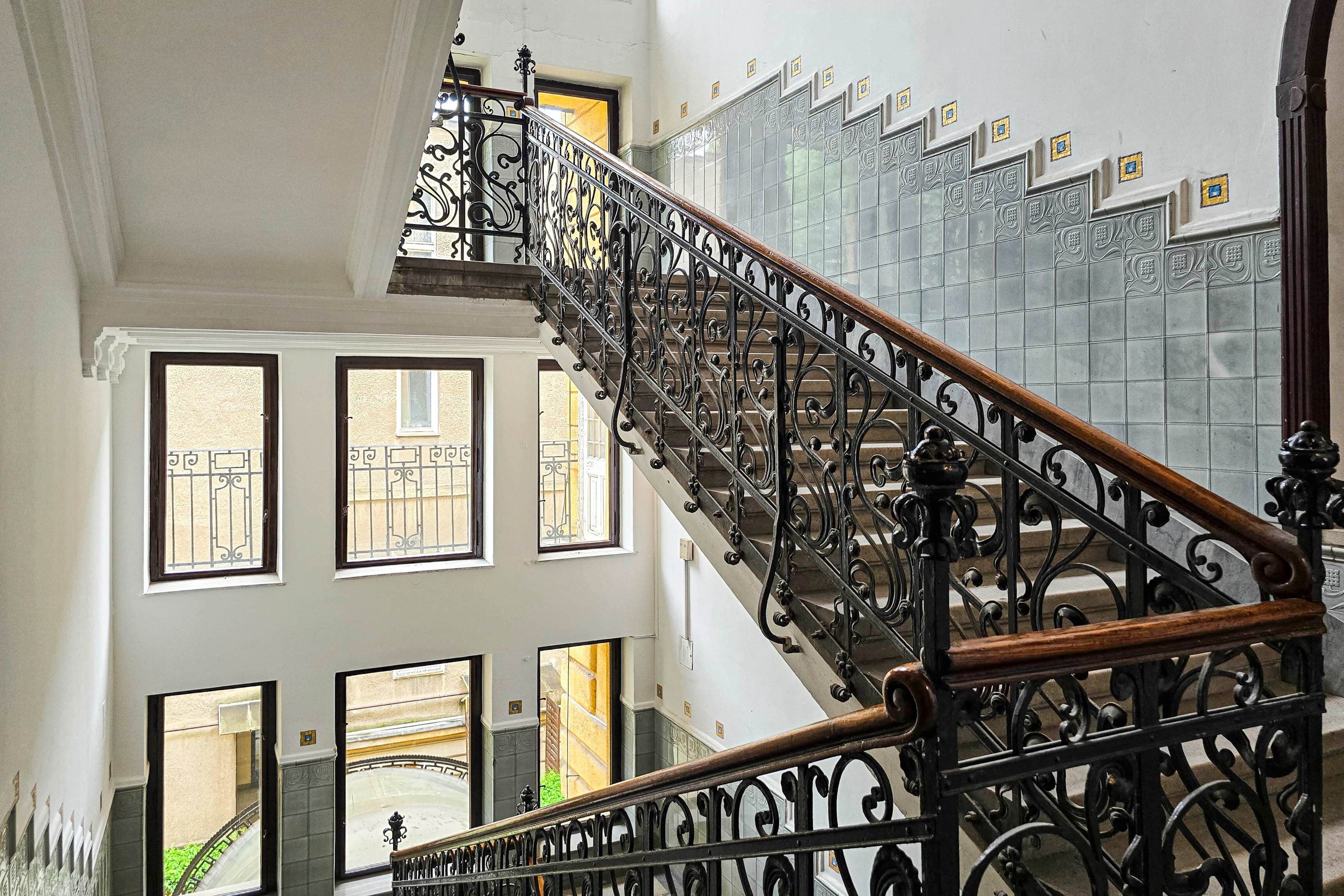 Eine Treppe mit aufwendiger schwarzer Metallgeländerung und einem hölzernen Handlauf.