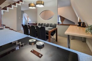 A modern kitchen with a central island, dining area with chairs, and a staircase. - Appartamento Quattroporte (Budapest)