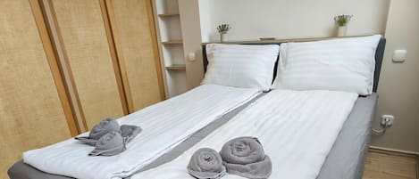 A double bed with grey and white bedding, two pillows, and two rolled towels.