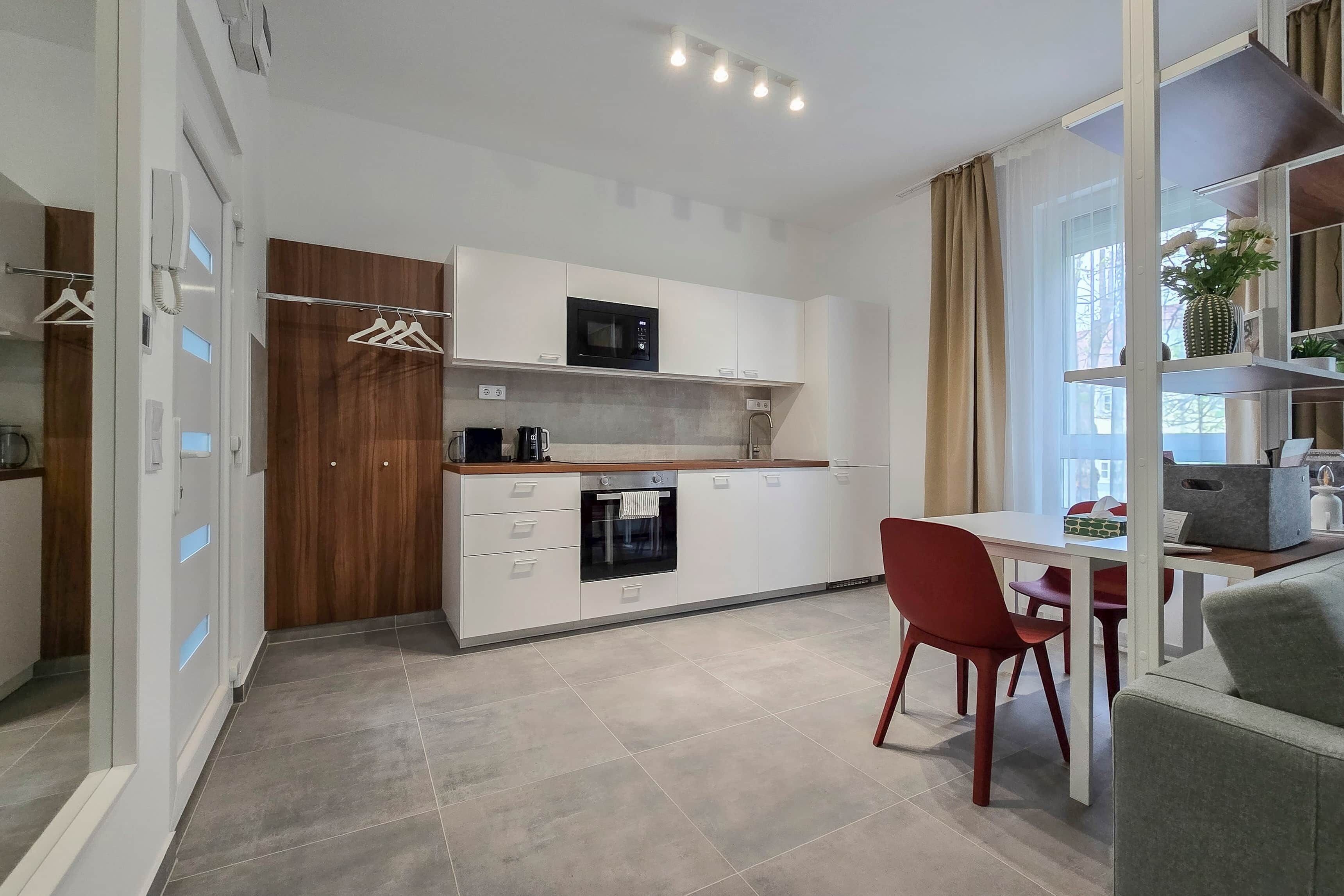 Una cucina compatta con forno a microonde, forno e un piccolo angolo ristoro con una sedia rossa.