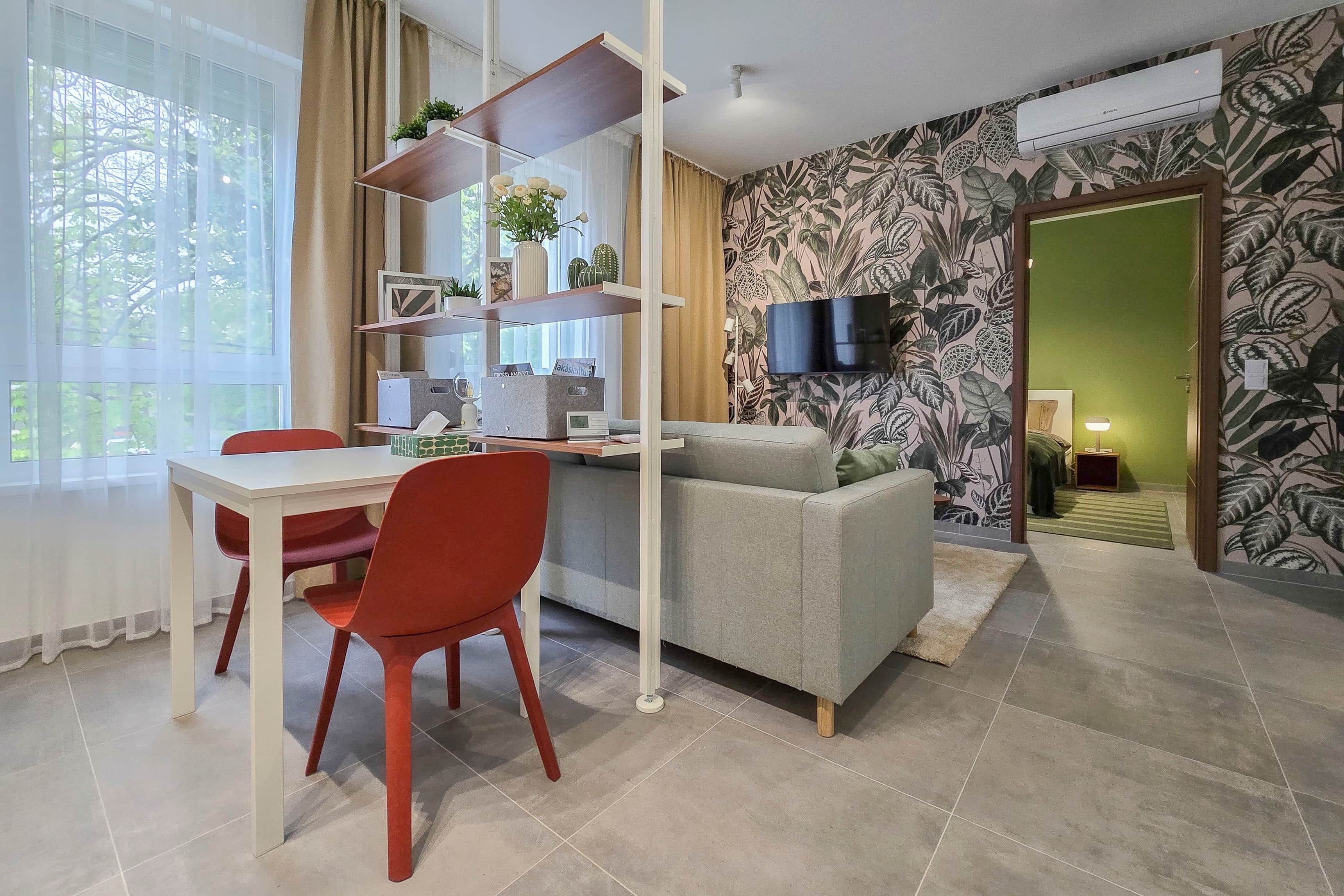 Una sala de estar moderna con un sofá, una mesa de comedor con sillas, un televisor montado en la pared y un ventanal con cortinas.