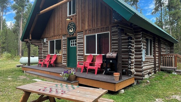 Una cabaña rústica de madera con un porche, sillas rojas y una mesa de picnic.