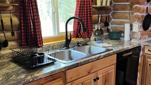 Una cocina de estilo rústico tipo cabaña con encimera de granito, armarios de madera, pileta de acero inoxidable y grifo negro.