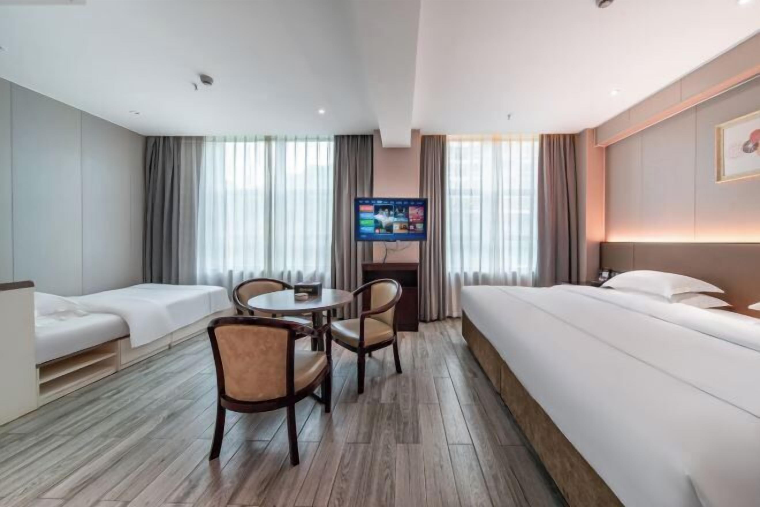 A hotel room with a bed, a desk with a chair, a TV, and a window with curtains.