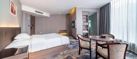 A hotel room with a bed, a desk, a chair, a small table, and a TV.