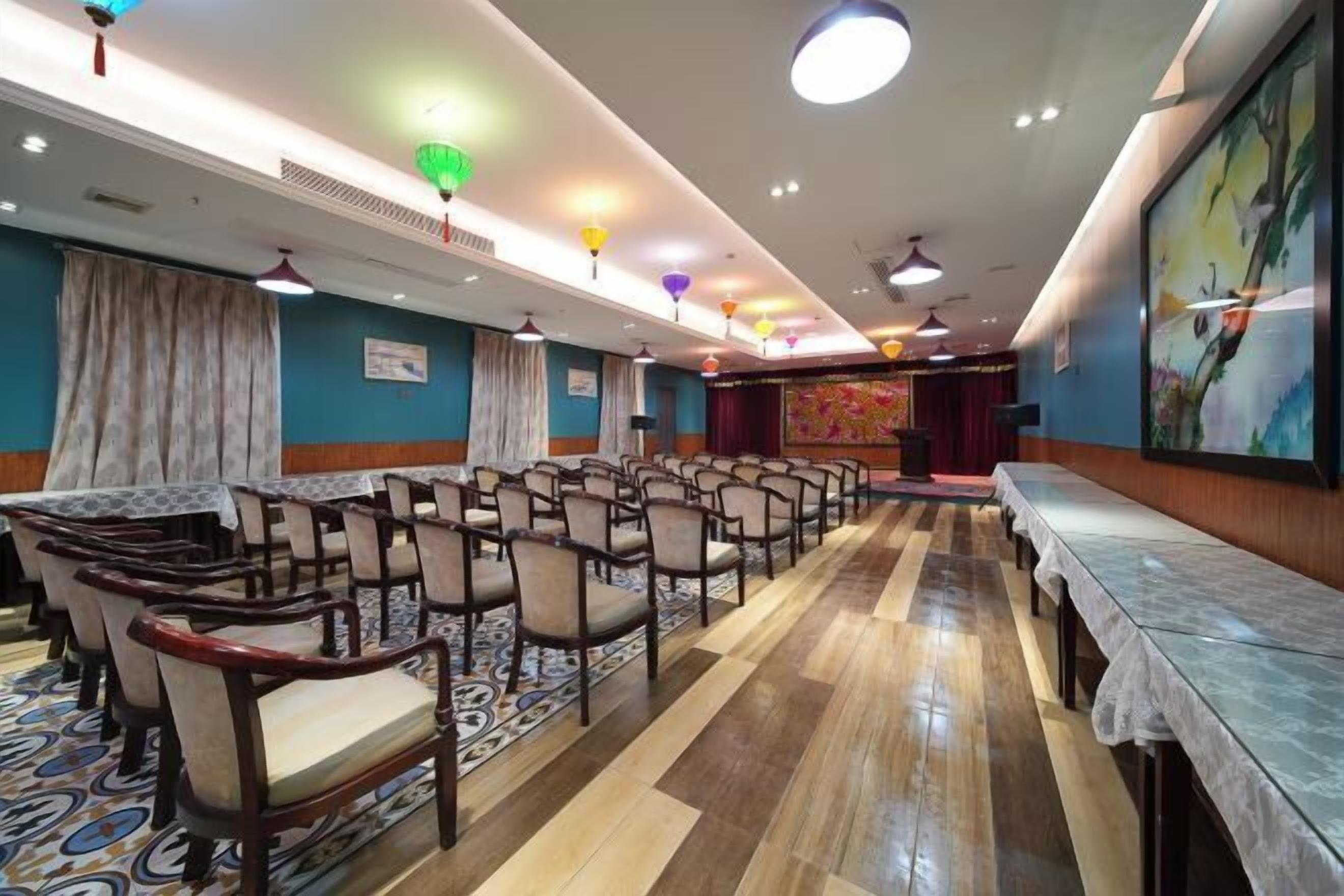 A conference room with rows of chairs, a long table, and a stage with curtains.