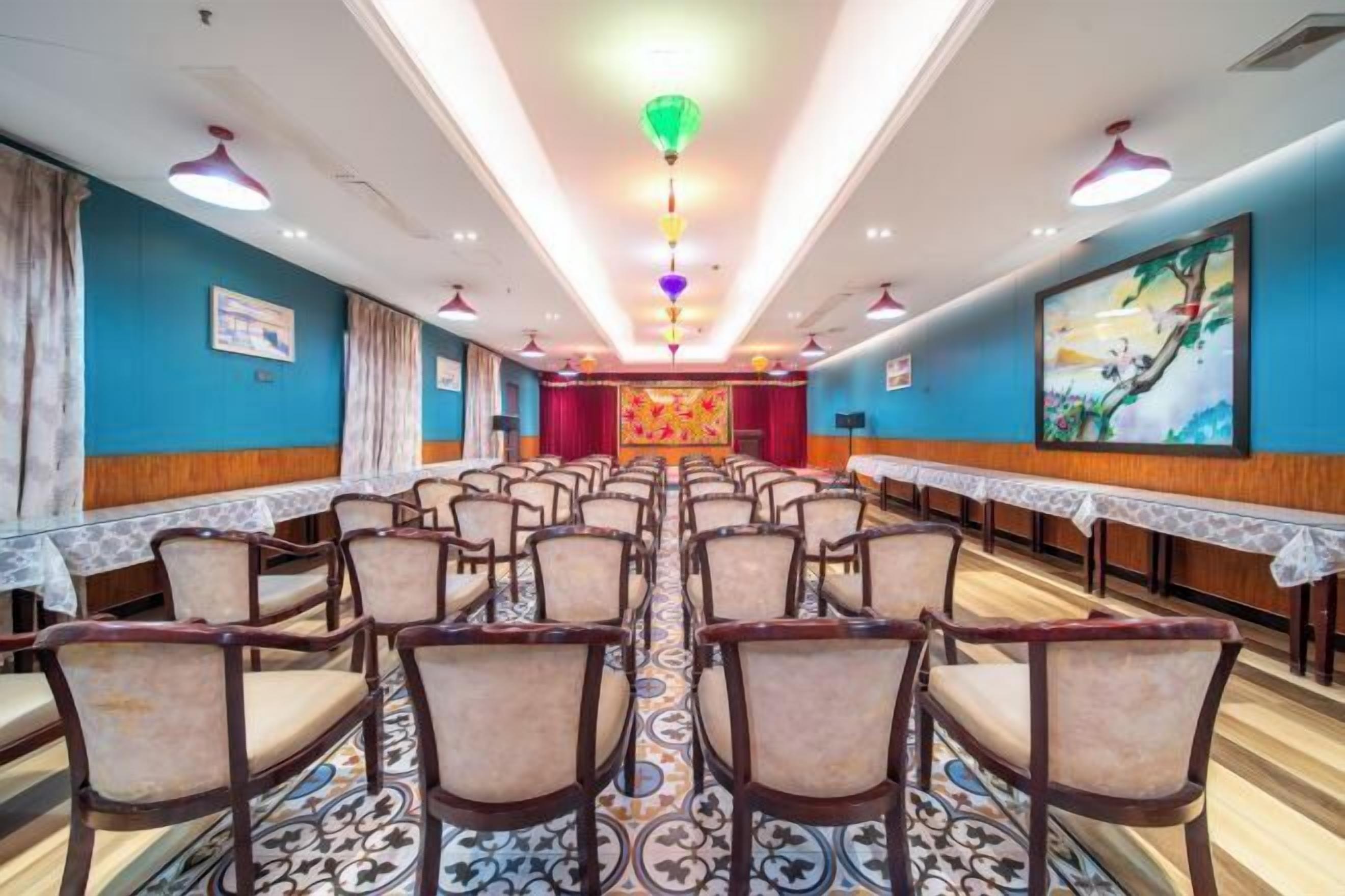 A conference room with rows of chairs and tables, a patterned carpet, and a colorful ceiling design.
