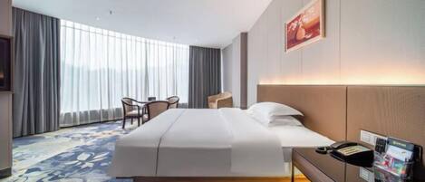 Een hotelkamer met een groot bed, een bureau met telefoon en tijdschriftenrek, een stoel en een groot raam met gordijnen.