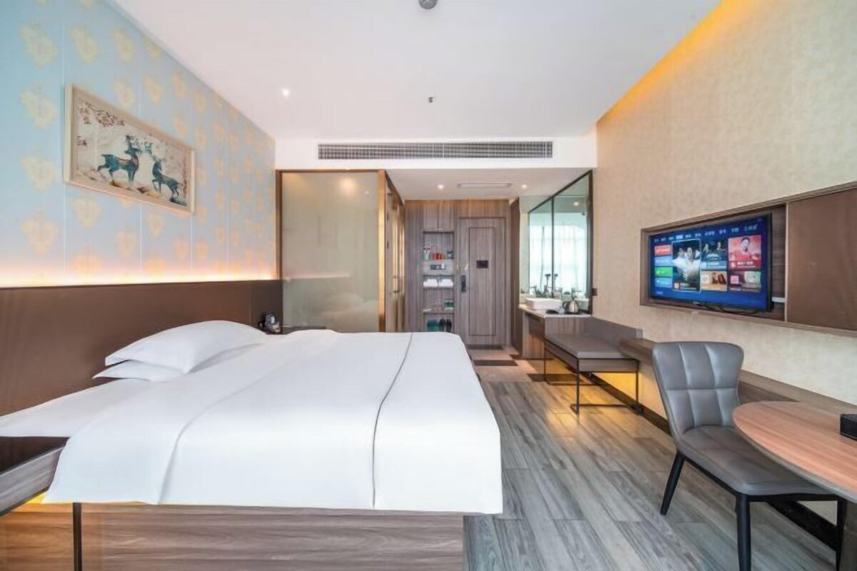 A hotel room with a bed, a desk, a chair, a TV, and a bathroom visible through an open door.