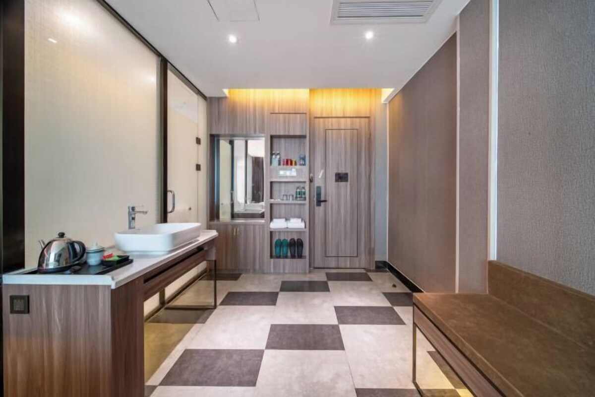 A modern bathroom with a large mirror, a sink, and a vanity. There is a shelf with toiletries and a bench.