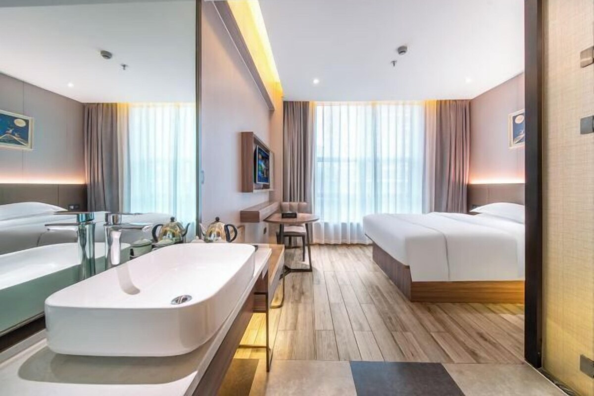 A modern hotel room with a large bathroom, a bed, a small table, and a seating area.