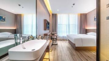 Une chambre d’hôtel moderne dotée d’une grande salle de bain, d’un lit, d’une petite table et d’un coin salon.
