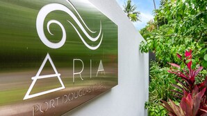 A sign with the name "ARIA" and "PORT DOUGLAS" on a metallic surface, surrounded by greenery.