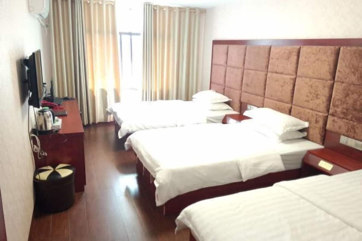 Habitación de hotel con tres camas, cabecera de madera, escritorio con silla y televisor.