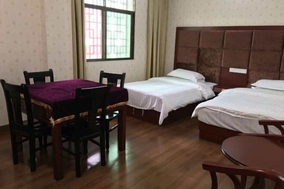 Una habitación con dos camas individuales, una mesa de madera con mantel púrpura y una ventana con cortinas.