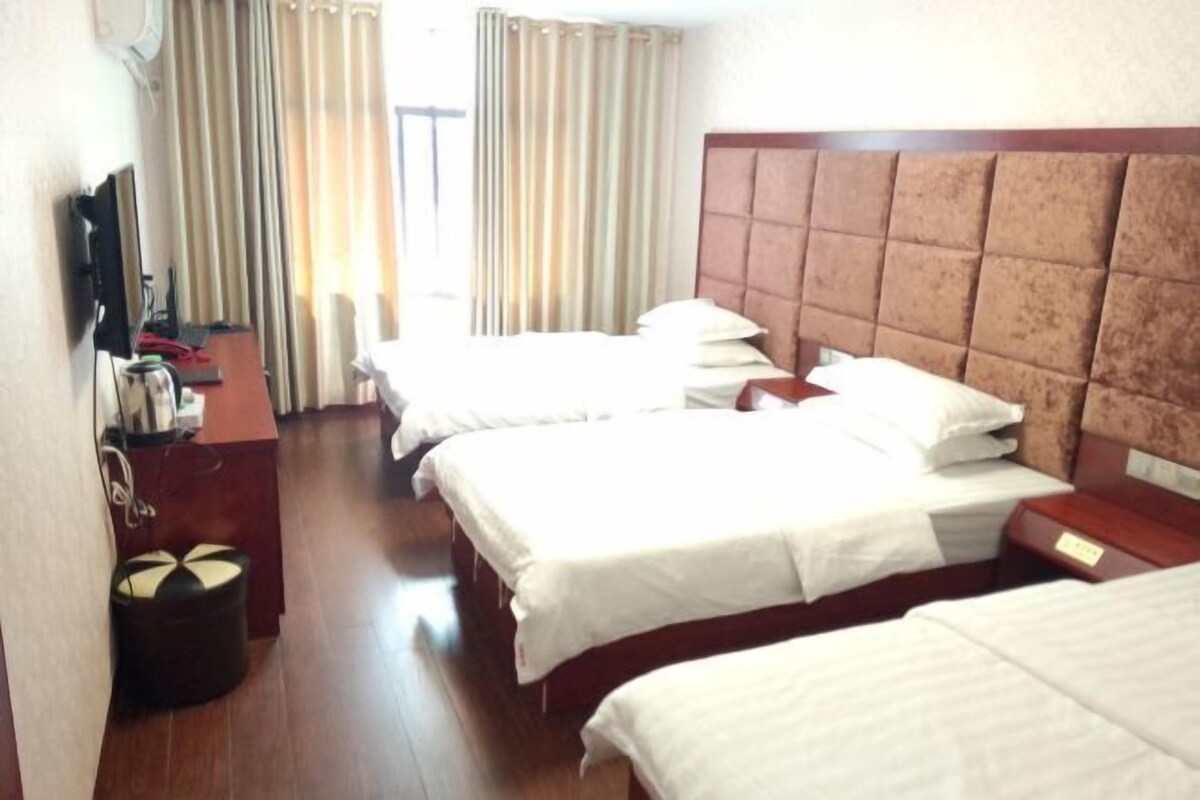 Ein Hotelzimmer mit drei Betten, einem Holz-Kopfteil, einem Schreibtisch mit Computer und einem Fernseher.
