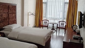 A hotel room with two beds, a wooden desk, a chair, a small table, and a window with curtains. - Caifu Business Hotel (Hengyang)