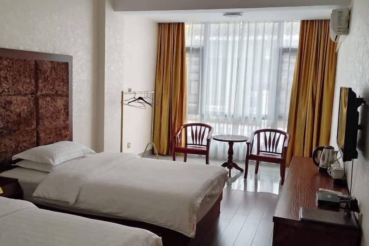Habitación de hotel con dos camas, un escritorio de madera, una silla, una mesita y una ventana con cortinas.