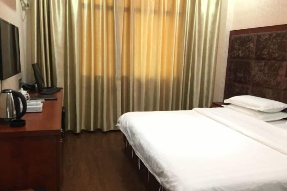 Habitación de hotel con cama, escritorio con hervidor, televisor de pantalla plana y cortinas.