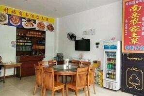A restaurant with a round table and chairs, a refrigerator, a TV mounted on the wall, and a shelf with condiments.