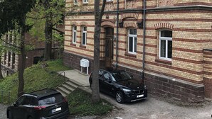 Un edificio storico con facciata in mattoni, numerose finestre e un'auto nera parcheggiata di fronte.
