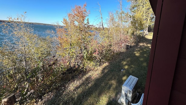 A view of a lakeside property with a wooden deck, a bench, and a clear blue sky.