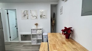 A modern kitchen with a wooden table, bench, and white cabinetry. There are three wall-mounted air conditioning units and a door leading to another room. - SI HOUSE - Lovely 2 bedroom unit in Staten Island (Staten Island)