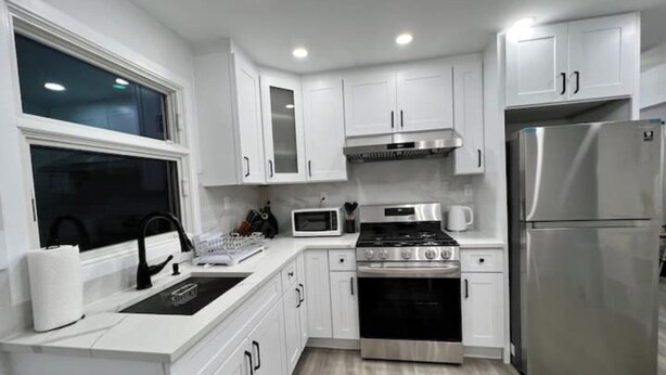 A modern kitchen with white cabinets, a stainless steel refrigerator, a stove, and a microwave. - SI HOUSE - Lovely 2 bedroom unit in Staten Island (Staten Island)