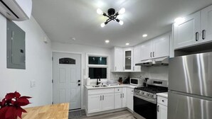 A modern kitchen with white cabinetry, stainless steel appliances, and a wooden dining table. - SI HOUSE - Lovely 2 bedroom unit in Staten Island (Staten Island)