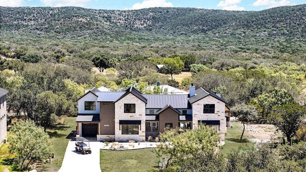 Une maison moderne à deux étages, dotée d’une façade en pierre, d’un garage et d’une allée.