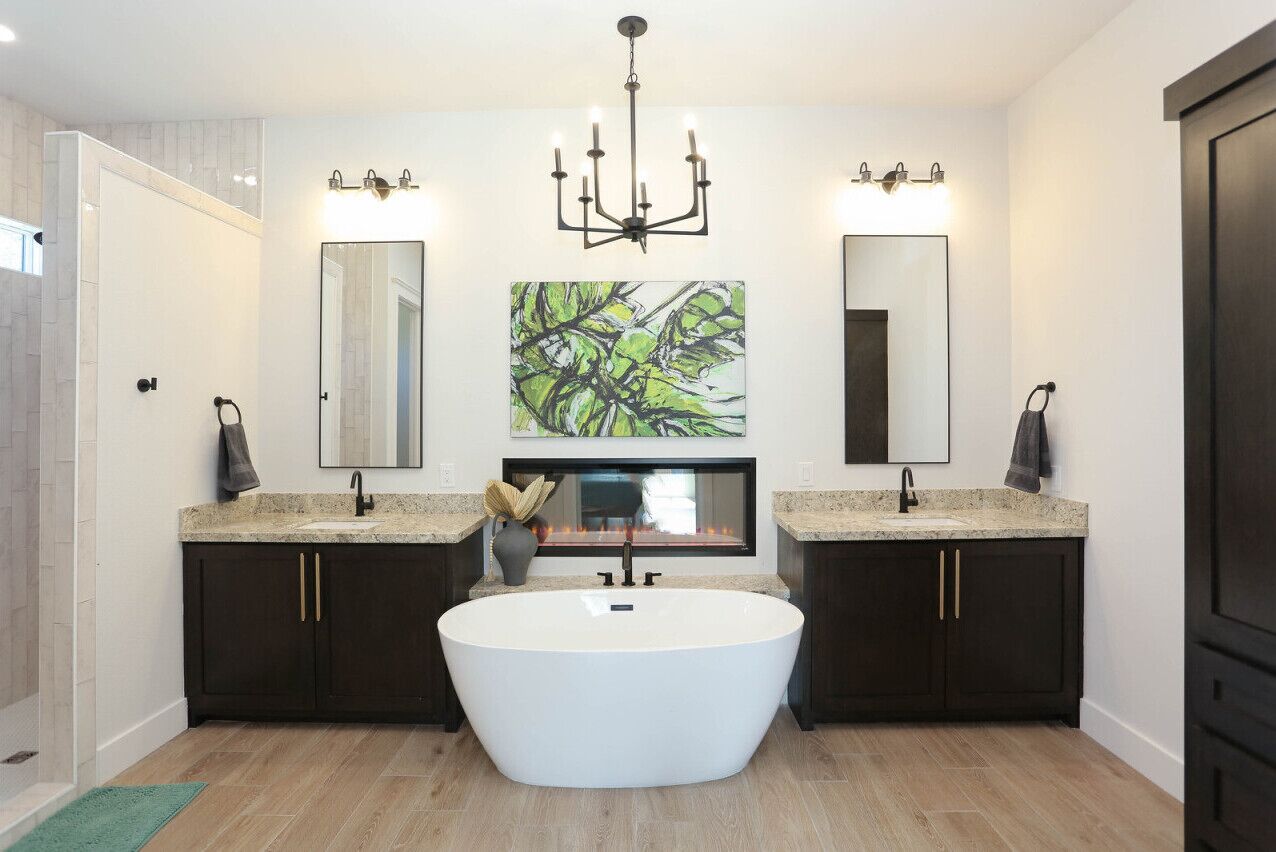 Un baño moderno con una bañera independiente, lavamanos dobles, muebles oscuros y un espejo grande sobre la bañera.