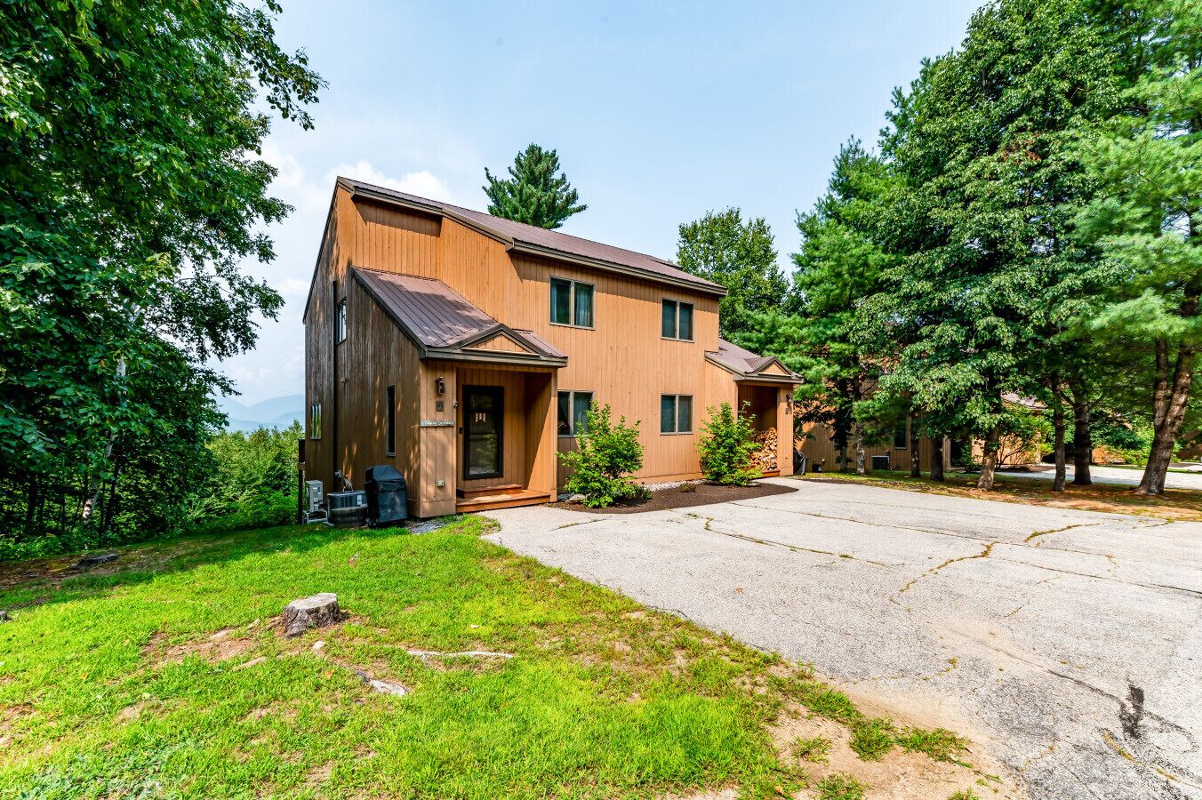 Une maison en bois à deux étages, dotée d’un porche à l’avant, d’une allée et d’une pelouse bien entretenue.