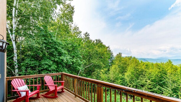 A wooden deck with two red Adirondack chairs and a metal railing. - Attitash Awesomeness - Fun for the Whole Family (Bartlett)
