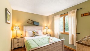 A bedroom with a wooden bed, two bedside tables, a window with curtains, and a wall-mounted shelf. - Attitash Awesomeness - Fun for the Whole Family (Bartlett)