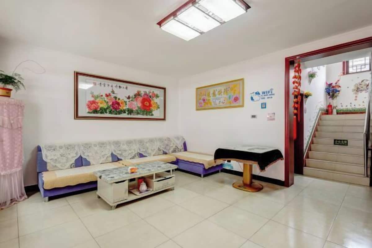 A room with a sofa, a small table, a bed, a staircase, and a wall with a framed picture and a poster.