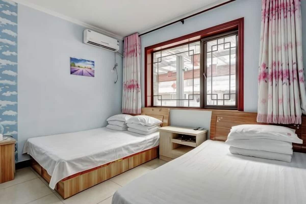 A bedroom with two beds, a desk, a window with curtains, and an air conditioning unit.