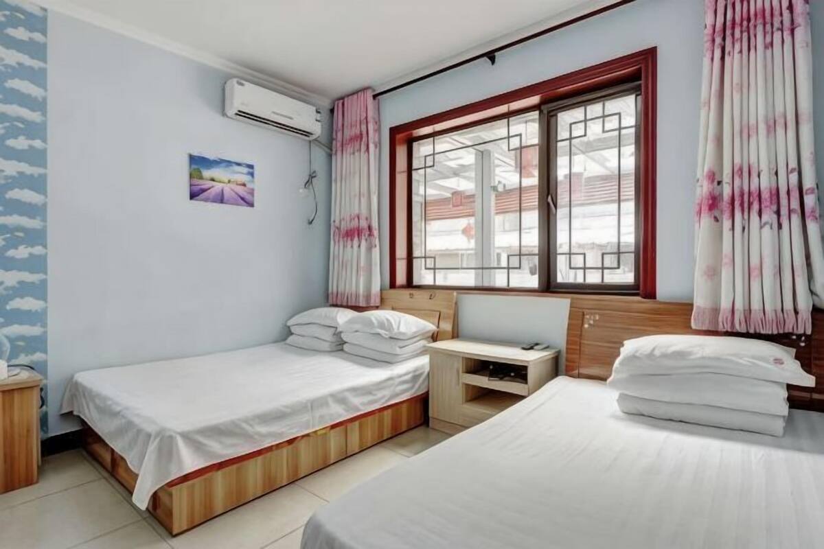 A bedroom with two beds, a desk, a window with curtains, and an air conditioning unit.