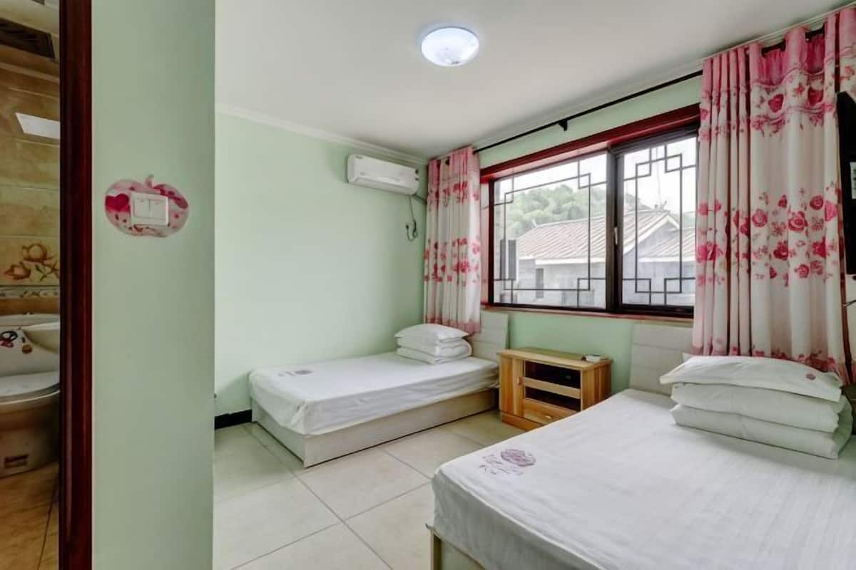 A room with two beds, a window with curtains, a wooden bench, and a wall-mounted air conditioner.