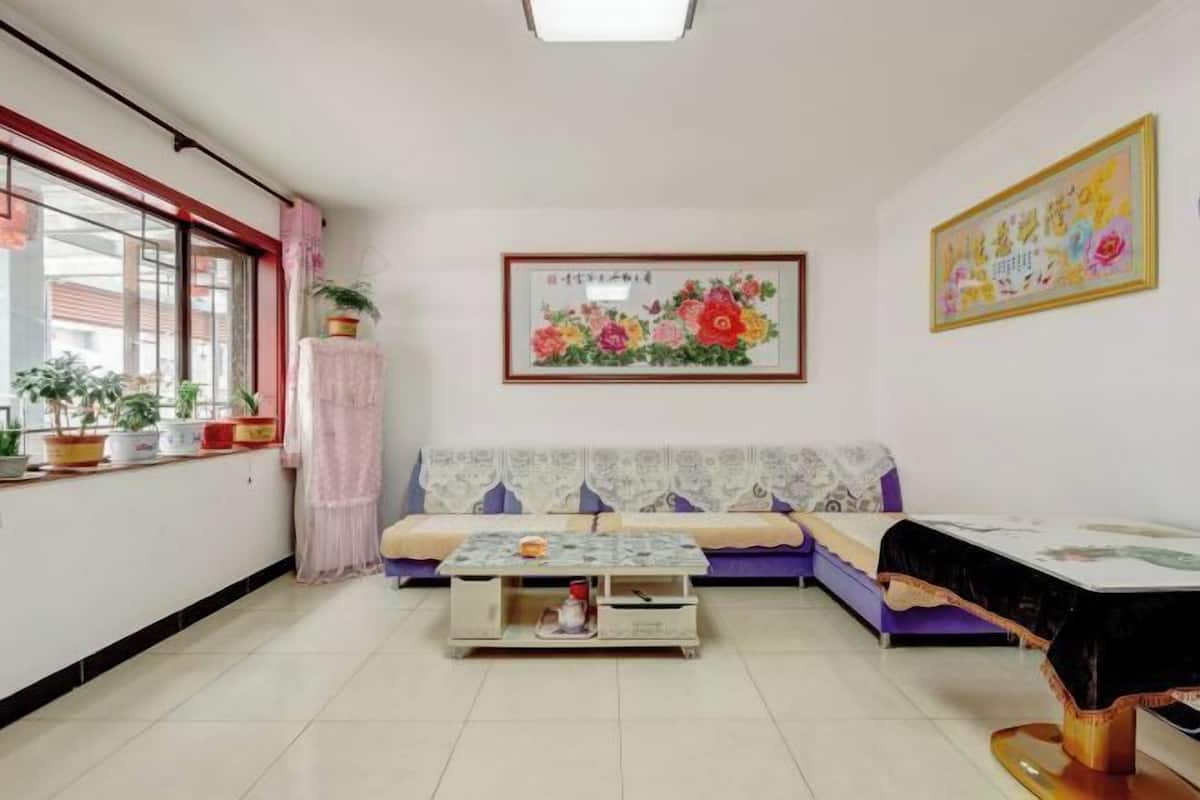 A room with a sofa, a coffee table, a window with plants, and artwork on the walls.
